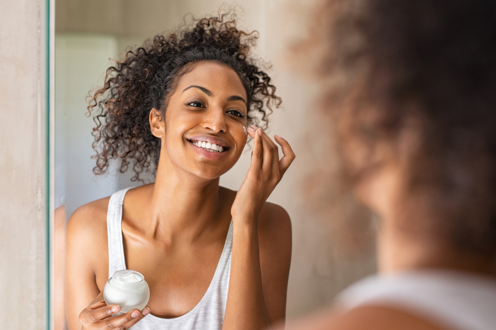 smiling woman applying moisturizer in mirror
