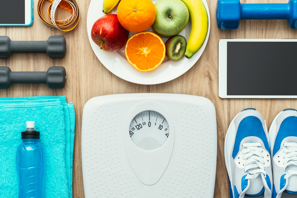 scale, exercise equipment, and healthy fruits spread out on wooden surface