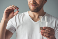 man holding supplement pill and glass of water