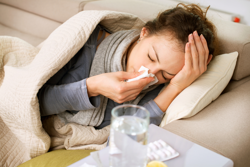 woman with flu lying on couch blowing nose